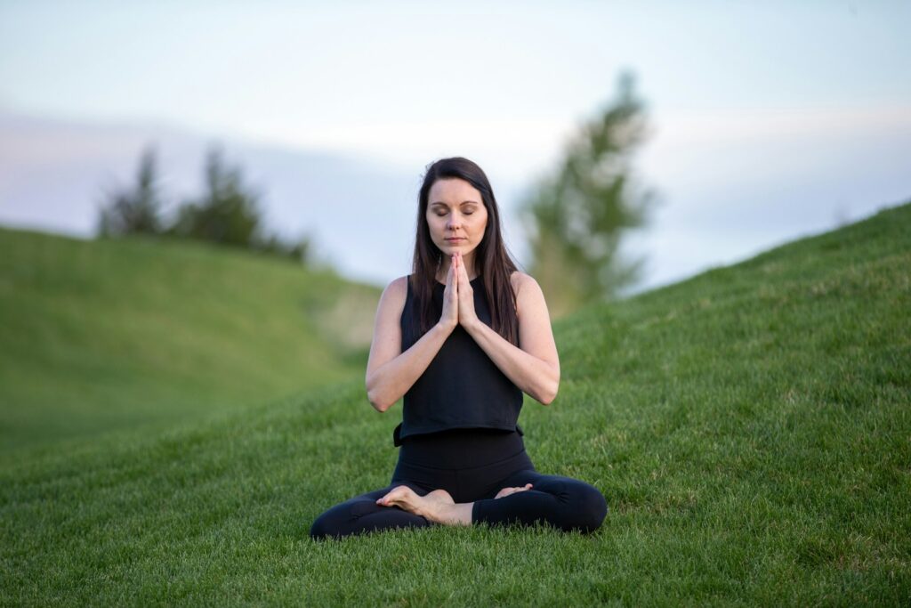 woman in black tank top and black pants sitting on green grass field and doing mindful meditation.